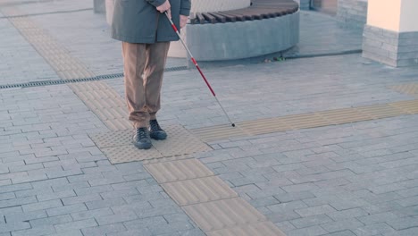 visually impaired man is walking on a tactile warning tile with the help of his cane. detectable warning surface for the vision impaired outdoors in the city.