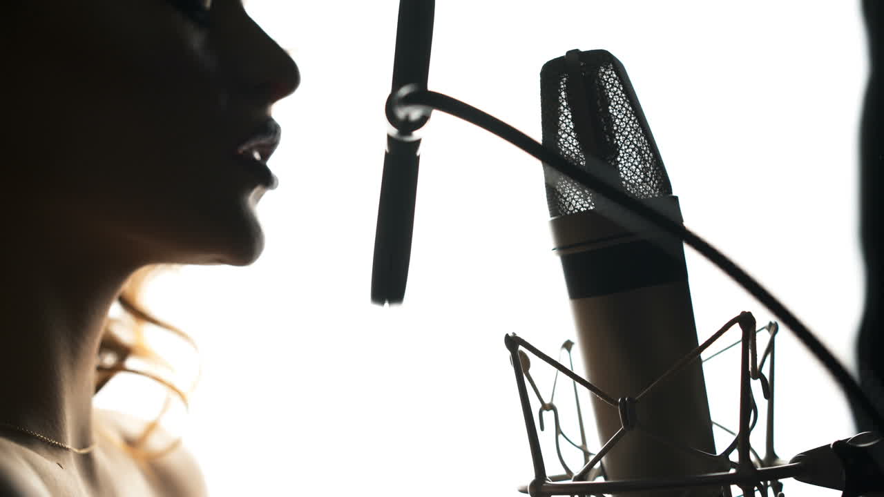 Beautiful woman singing into a microphone in a recording studio. Black and white. Female silhouette