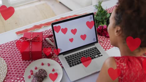 animation of heart icons over african american woman using laptop with copy space, slow motion