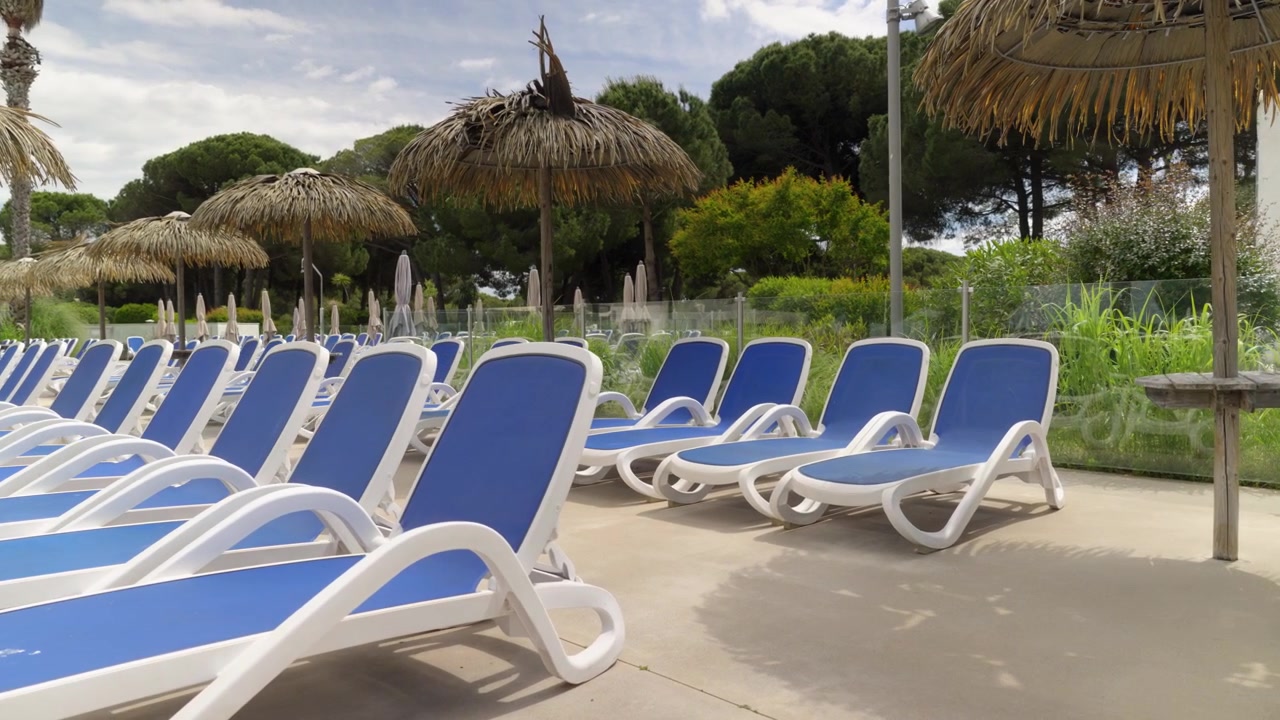 Empty blue sun loungers by a glass pool fence at a holiday club outdoor area
