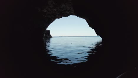 look out to the horizon from the inside of a dark sea cave with the sky reflecting in the water, vis island, adriatic sea, croatia