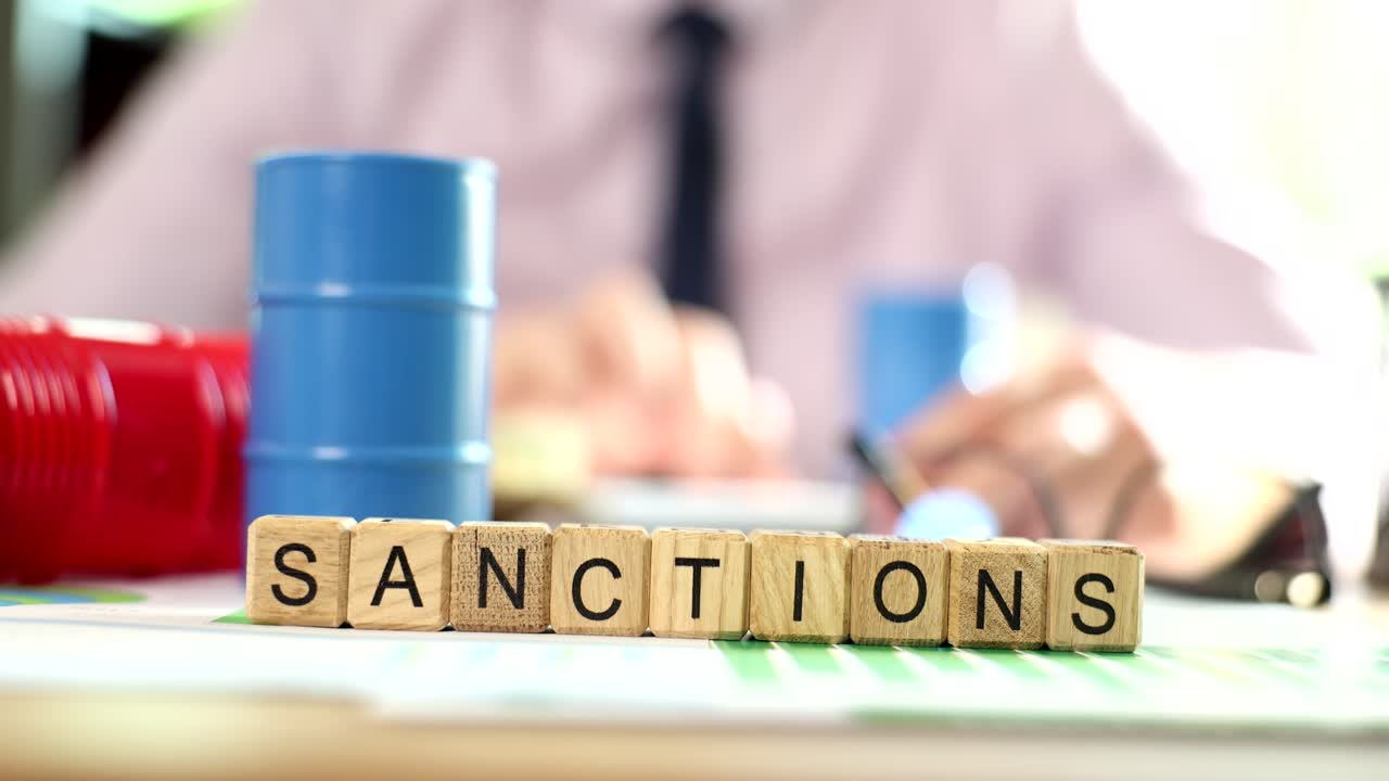 Word with the sanction of oil barrels and financial documents on table and business man considers
