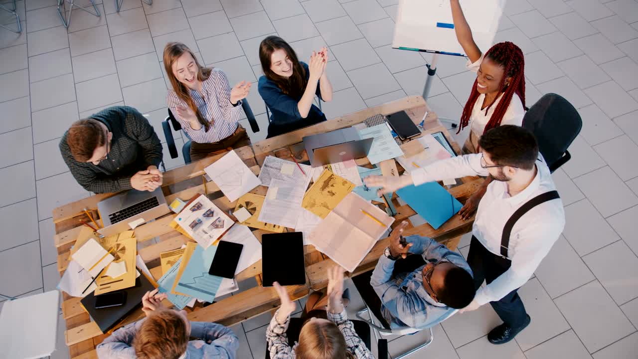 Top view happy team of colleagues working together at modern office, joining hands and clapping, celebrating success.