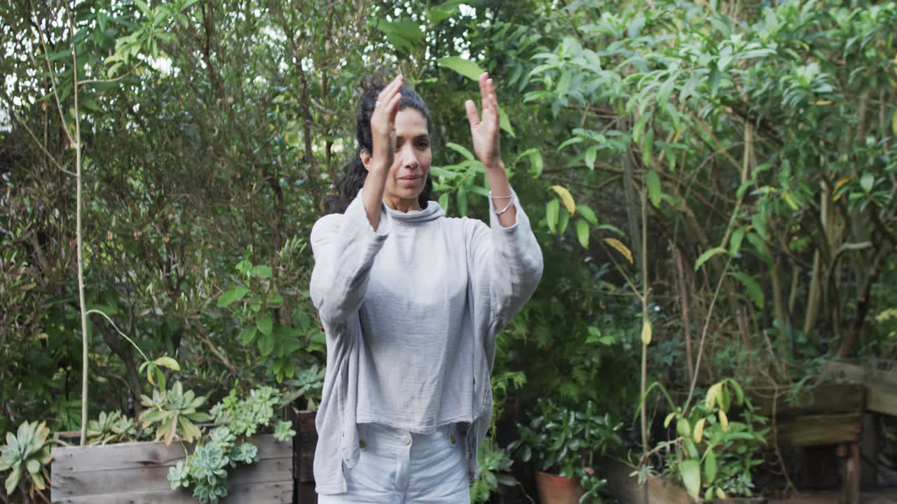 concentrada mujer biracial practicando yoga en el jardín soleado, cámara lenta