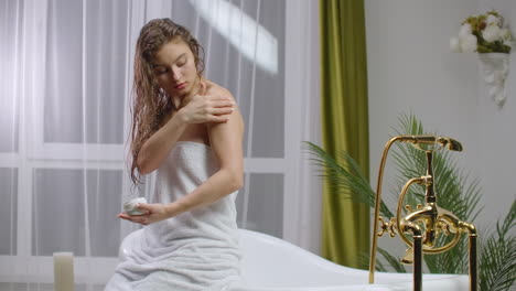 beauty and body care female elbow pain and health care concept. slow motion of caucasian woman applying lotion cream moisturizer relaxing in bed in white cozy apartment near window. hand touching careful