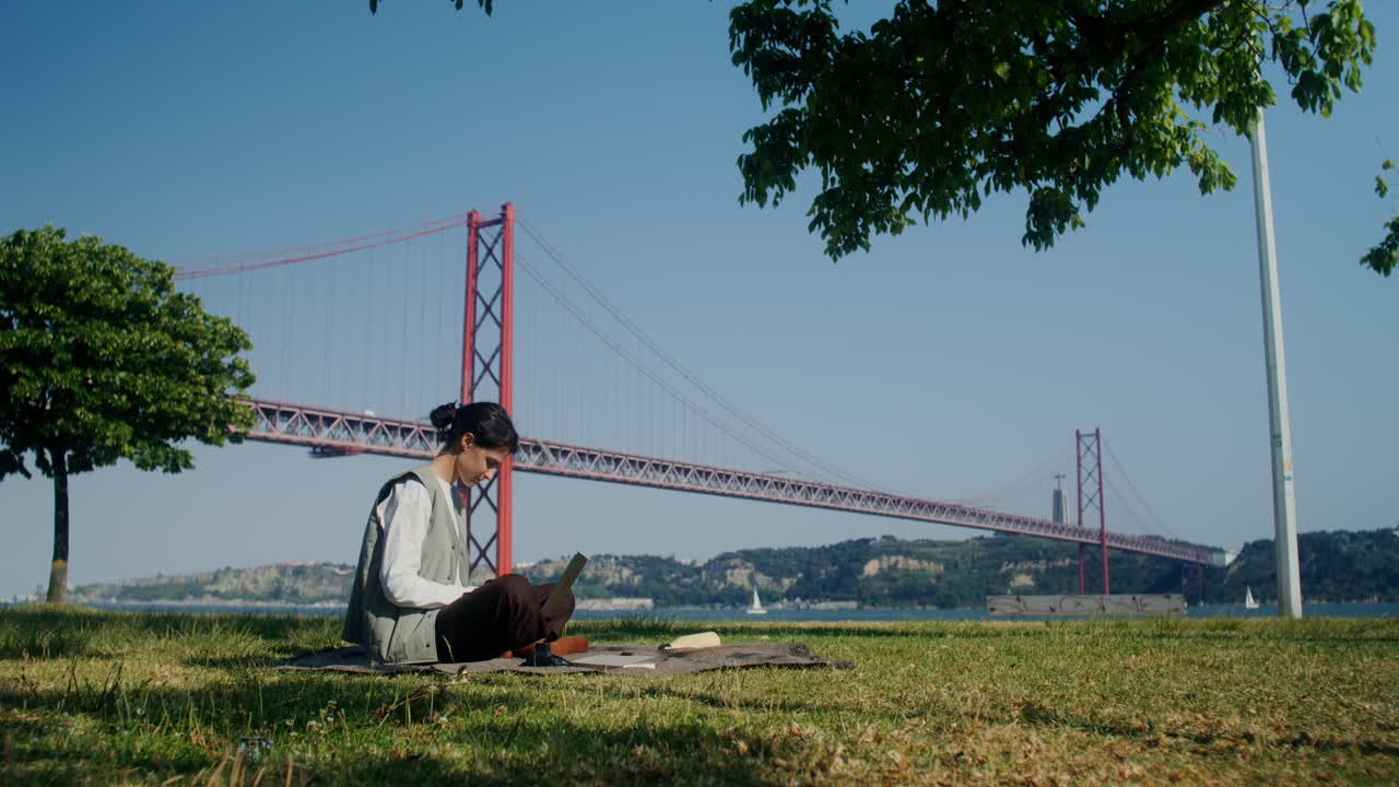 배경 에 다리 가 있는 공원 에서 노트북 을 사용 하고 있는 여자