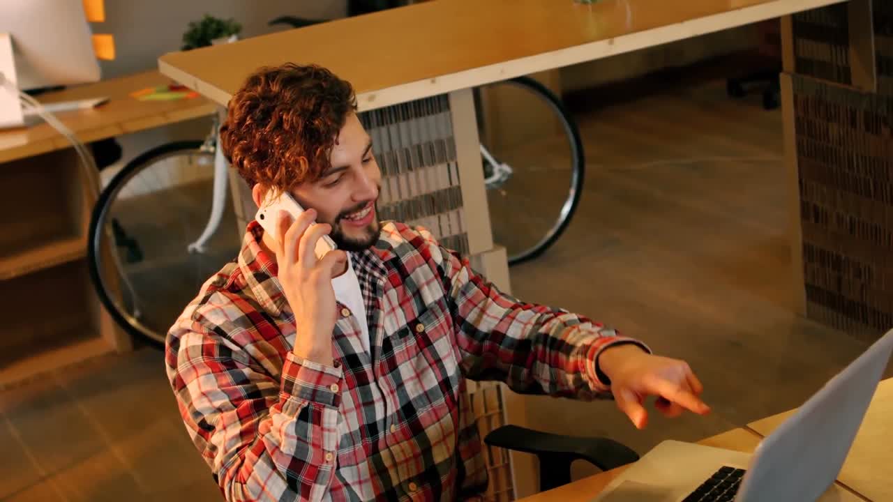 Graphic designer talking on phone while working on laptop