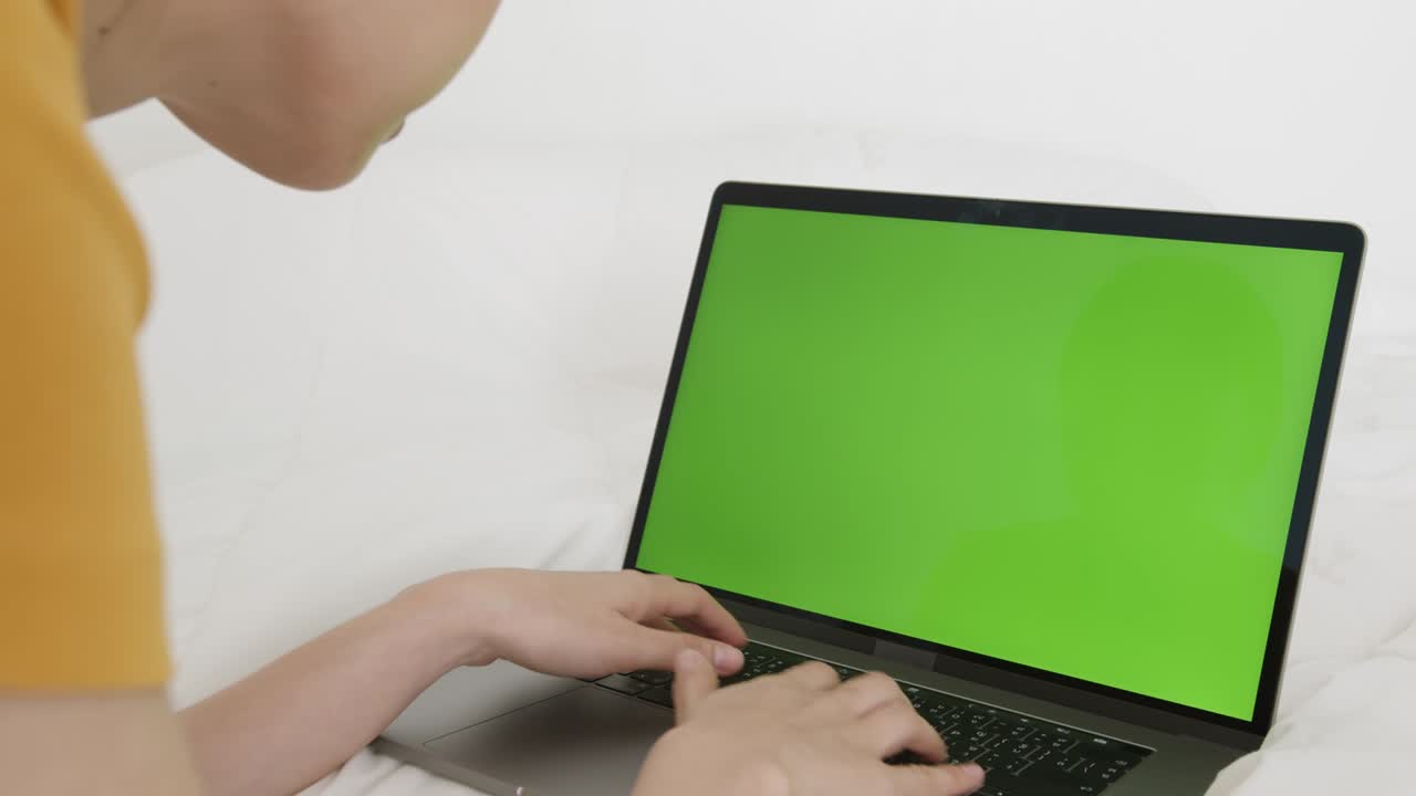 una mujer usando una computadora portátil con una pantalla verde en la cama de su casa.
