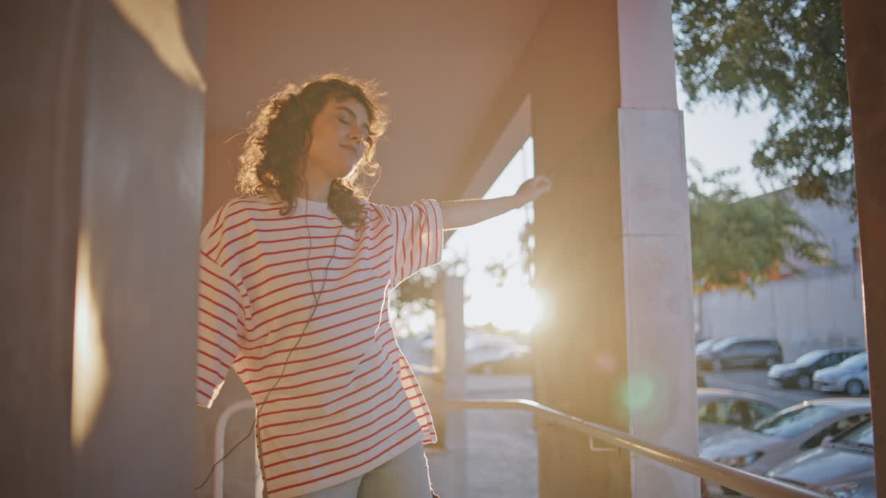 무관심한 십대가 해가 지는 도시 거리에서 헤드폰을 들고 춤을 춘다. 여자가 음악을 듣고 있다.