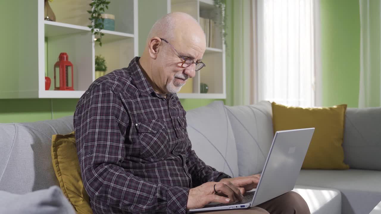 Old man sitting on sofa at home using laptop fun and happy.