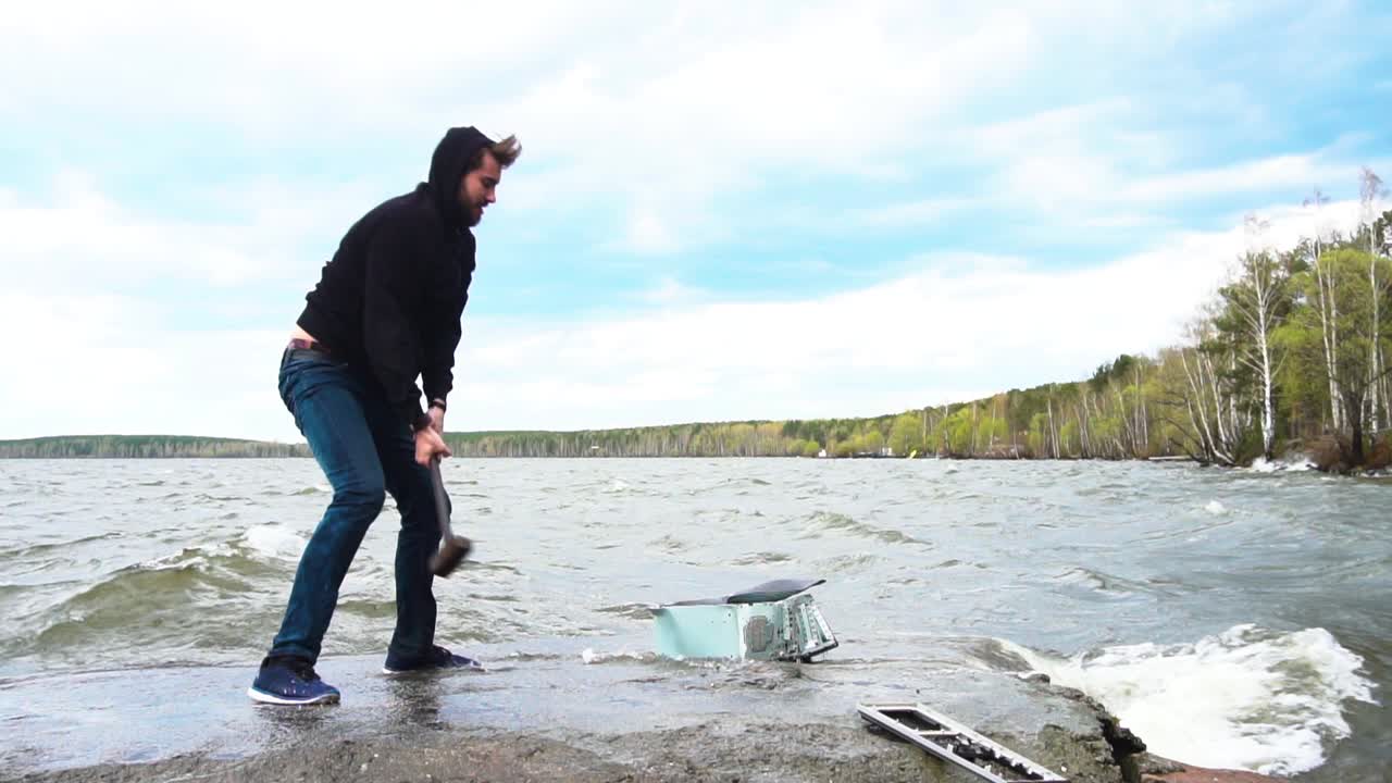 해변에서 망치로 컴퓨터를 파괴하는 남자