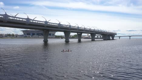 aerial drone tracking shot of two people riding a kayak under the western high-speed diameter bridge, gulf of finland in saint petersburg, russia