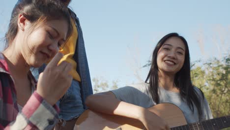close up asian teen group singing, sitting play a guitar at campsite in the summer time