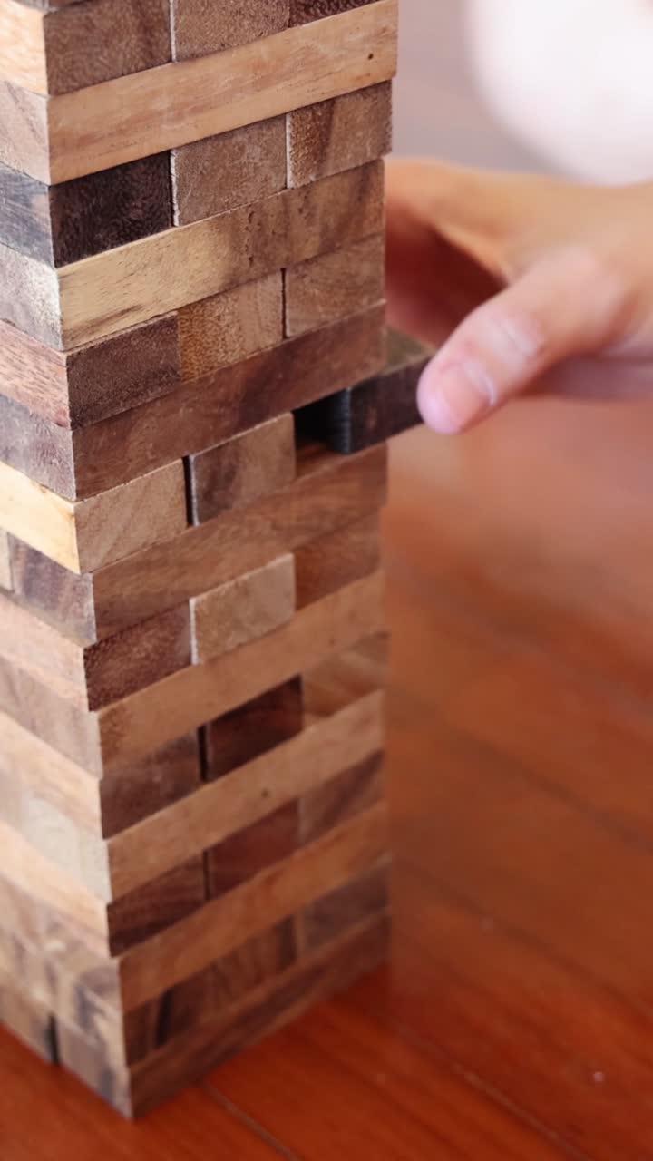 La mano di una persona fa scivolare con attenzione un blocco di legno scuro da una torre alta e impilata