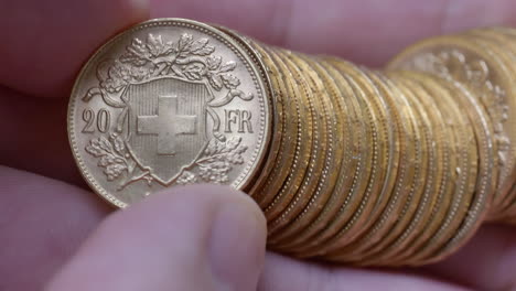 macro shot of person checking several rare golden vreneli francs in hand