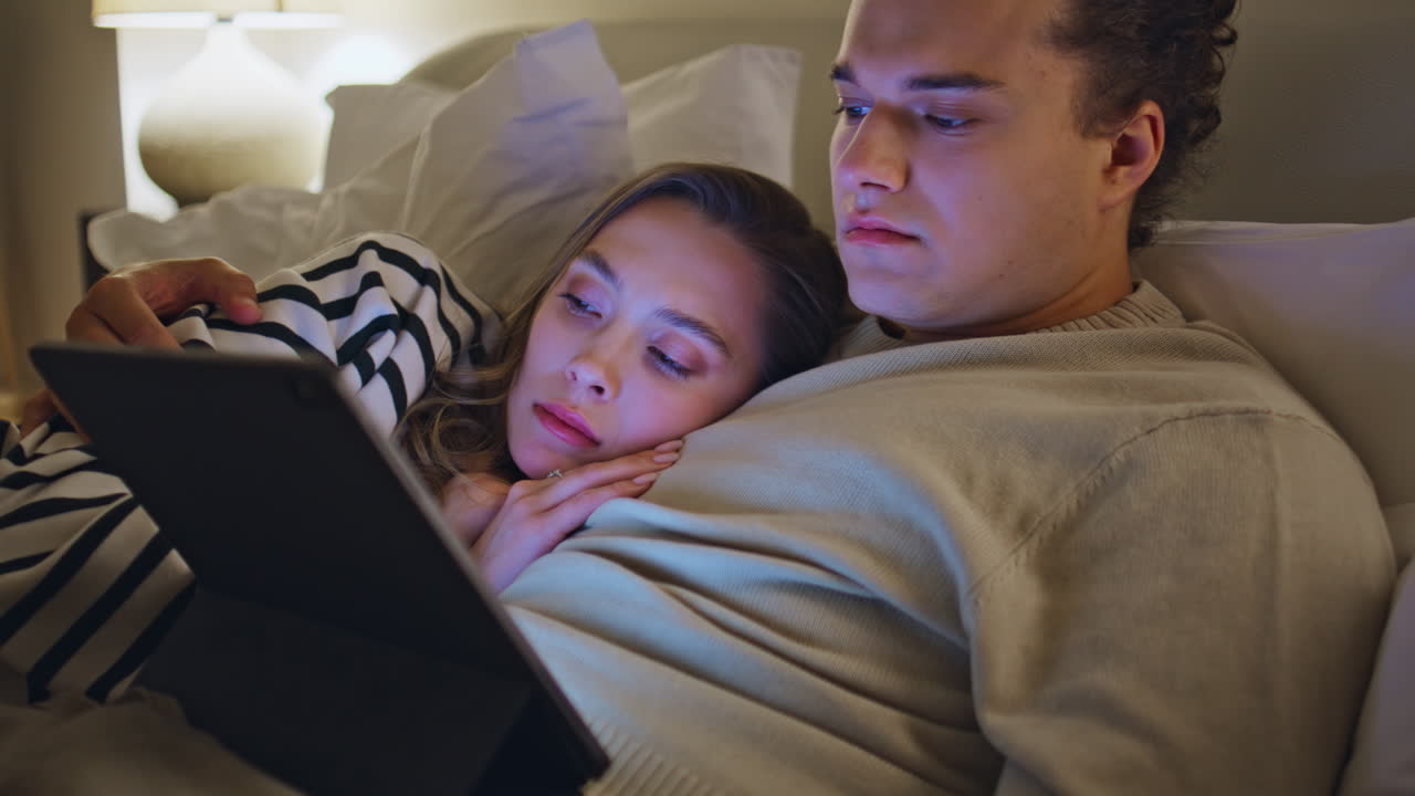 Love couple lying bed focused on watching tablet closeup. Romantic spouses