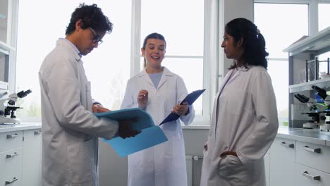 International-Group-of-Scientists-in-Laboratory.science-research,-work-and-people-concept-international-group-of-happy-scientists-with-clipboards-discussing-report-in-laboratory