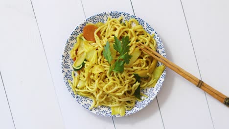 traditional noodles with chicken and vegetables served on ceramic plate with chopsticks on side