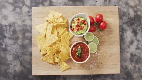 Close-up-of-nachos-and-sauces-on-wooden-tray-on-black-surface