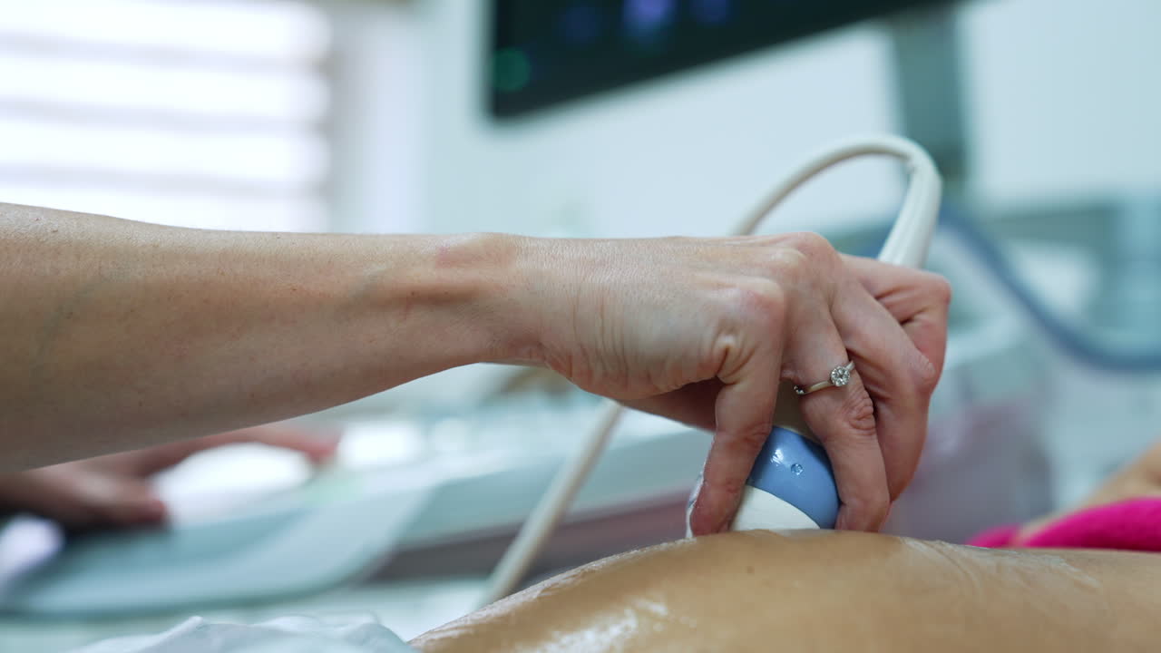 Hand of unrecognized female doctor holding device on the belly of woman. Pregnant lady is checked on ultrasonic machine. Close up.