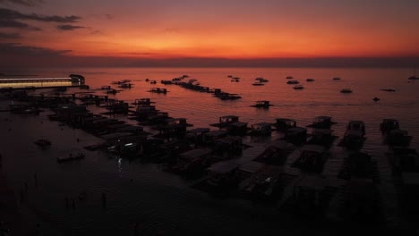 Toma-Aérea-Que-Muestra-La-Silueta-De-Barcos-Flotantes-De-Madera-En-La-Costa-Durante-La-Hora-Dorada.