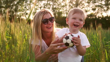 the concept of a happy family. close-up of a boy and his mother in a field with wheat spikes smiling and playing with a soccer ball