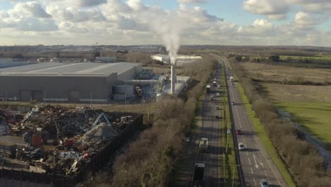 Aerial-strafing-shot-over-factory-and-smoking-chimney,-A12-major-road