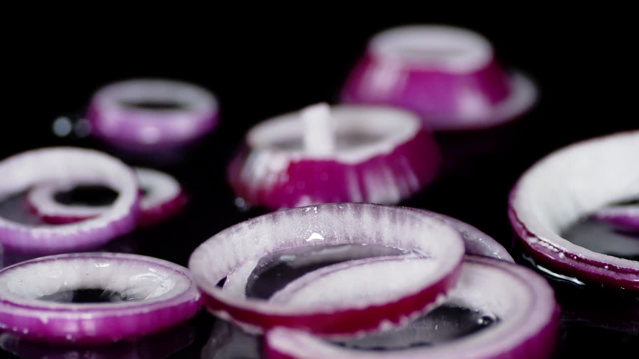 anillos de cebolla roja fresca caen sobre el agua con salpicaduras.