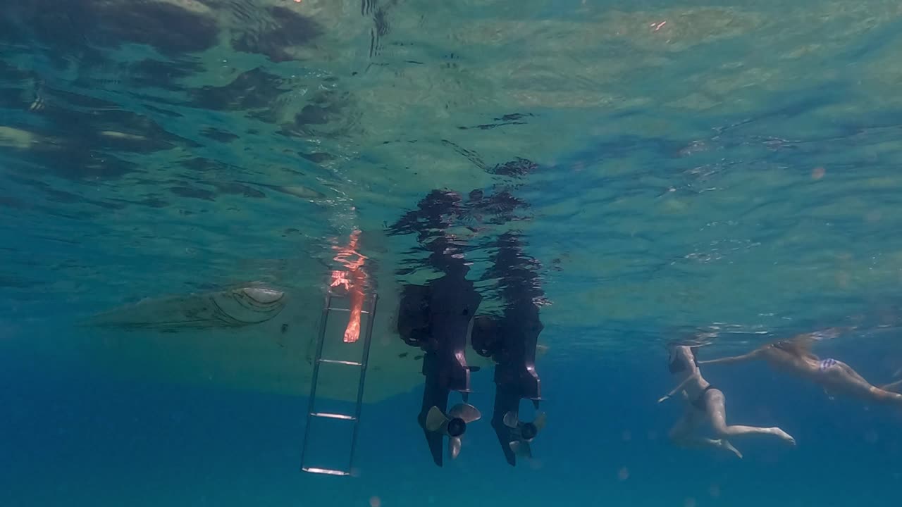 imágenes en cámara lenta bajo el agua de piernas y pies en agua de mar debajo de la superficie colgando de la escalera de la lancha motora