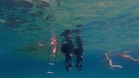 Slow-motion-under-water-footage-of-legs-and-feet-in-sea-water-beneath-surface-hanging-from-motorboat-ladder