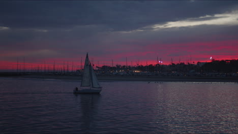 Sailboat-returning-to-harbor-at-dusk-with-amazing-colorful-sunset-behind