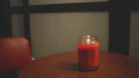 Red-Lit-Candle-With-A-Shimmering-Flame-On-Top-Of-Table-Next-To-A-Chair