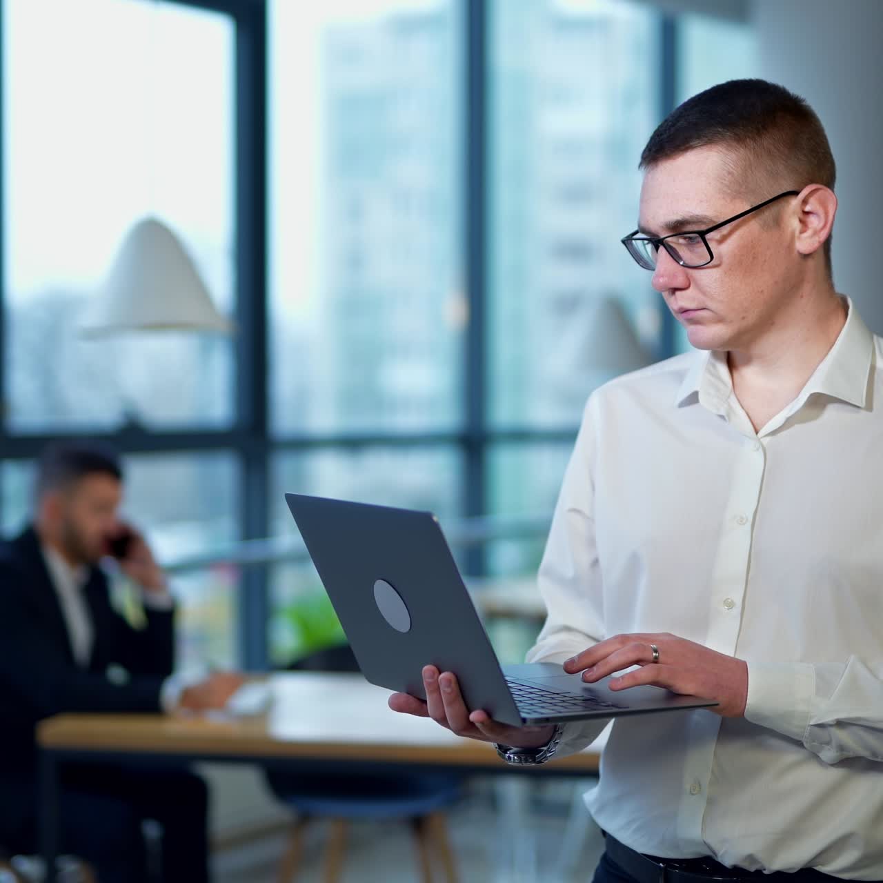 Man in a white shirt standing and holding laptop. Middle-aged male employee printing something on a computer keyboard. Man in blur at the backdrop