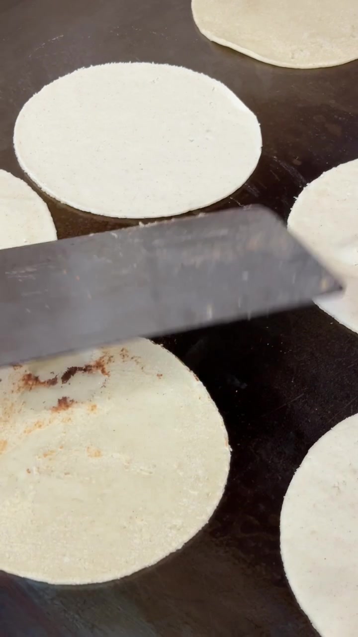 Vista ravvicinata dall'alto di tortillas di mais bianco fatte a mano che cuociono su un comal caldo mentre il vapore forma bolle e macchie tostate sulla focaccia rotonda fresca in una cucina tradizionale.