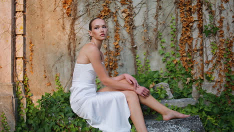 gorgeous model posing autumn foliage on old wall. elegant woman sitting stones