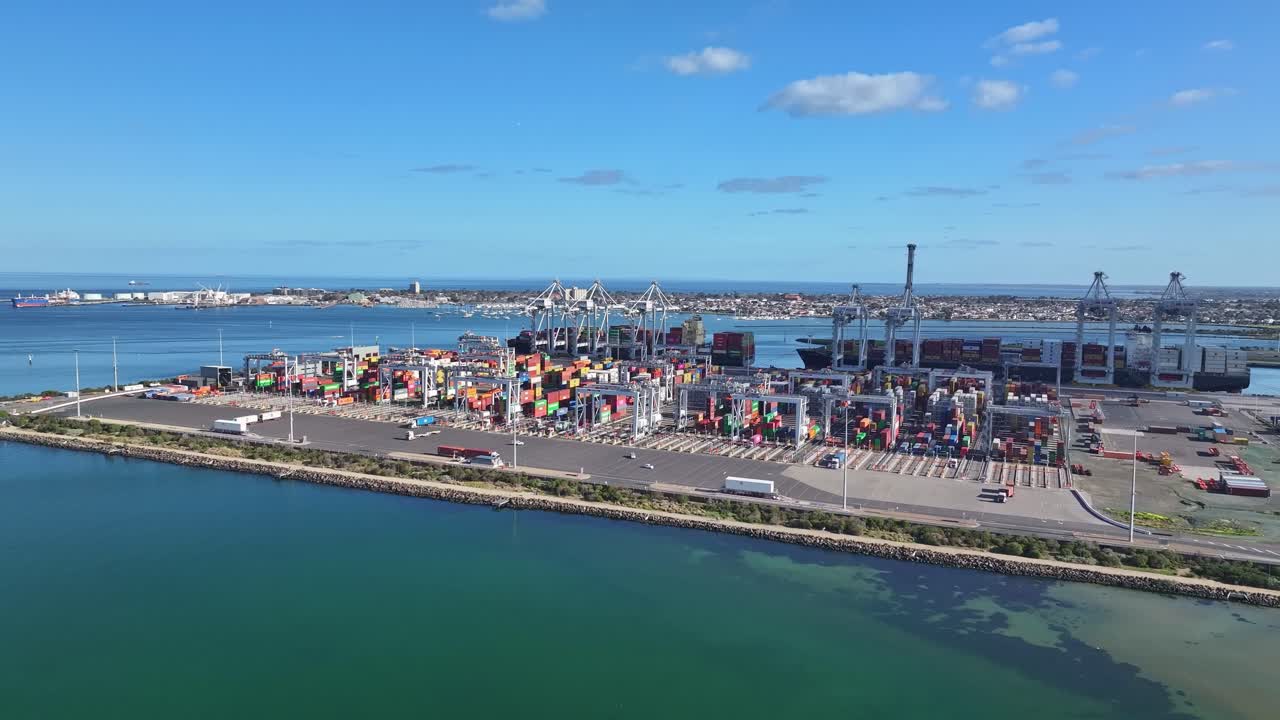 Containers and cranes at busy Melbourne shipping terminal beside blue coastal waters