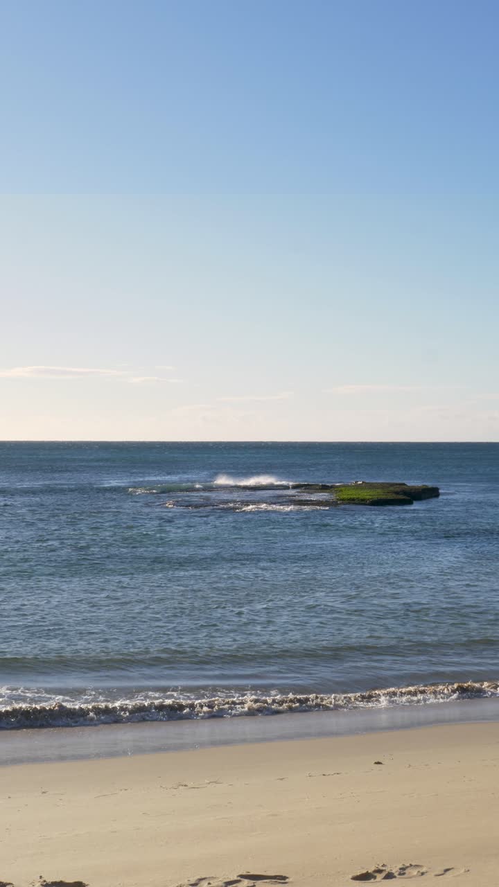 Portrait slow motion view of sea swell breaking on a sandy beach coastline with rock reef formations and clouds in the sky on the horizon at Bateau Bay Central Coast Australia travel nature outdoors