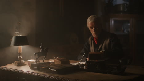 older passionate man evaluates an old watch in his office at night