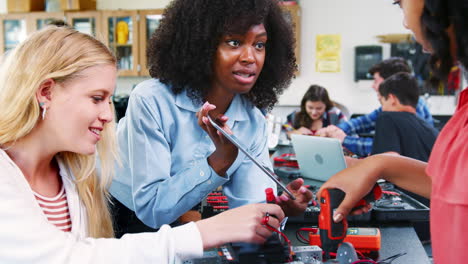 high school teacher with female pupils building robotic vehicle in science lesson