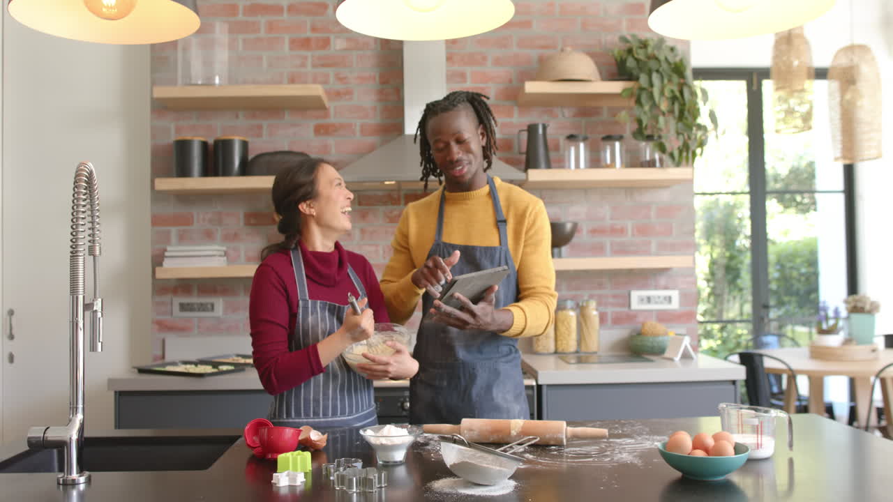 pareja feliz en delantales usando tableta y hornear en la cocina, espacio de copia, cámara lenta