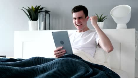 hombre ganador excitado usando tableta en la cama