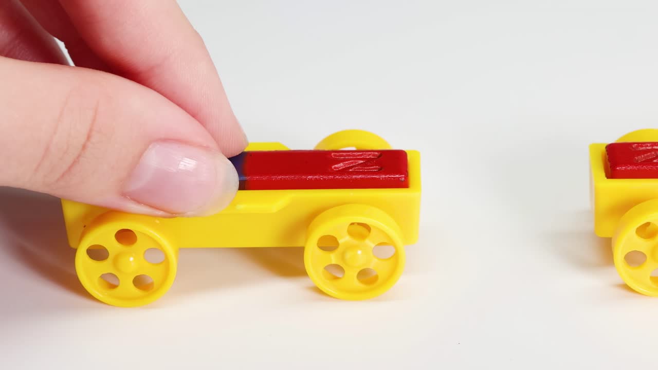 Hands manipulate yellow toy cars with red and blue magnets on a white surface.