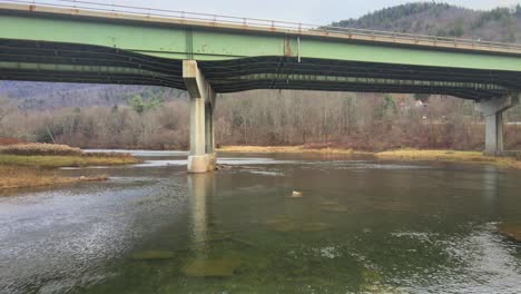 a drone flying under a bridge that's crossing a river, then flying higher above a river valley