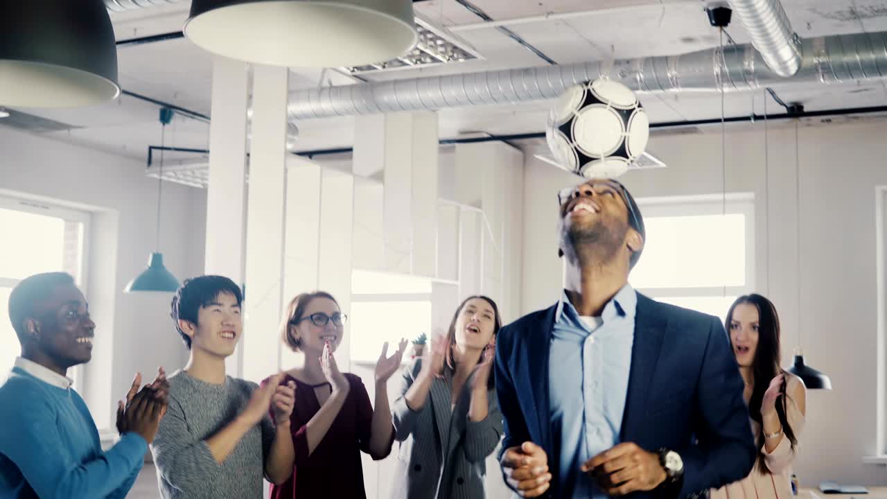 feliz director ejecutivo afroamericano haciendo malabarismos con la pelota en la cabeza. ejecutivos de negocios multiétnicos la gente celebra el éxito en la oficina 4k