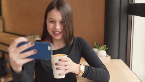 beautiful girl sitting in a restaurant and drinking coffee while video chatting on her phone