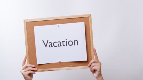 Woman's-hand-shows-the-paper-on-board-with-the-word-Vacation-in-white-studio-background-with-copy-space