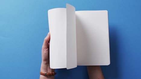 close up of hand leafing through book with copy space on blue background in slow motion