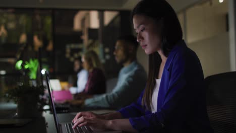 Video-of-asian-businesswoman-and-diverse-colleagues-at-desks-using-computers-at-night-in-office