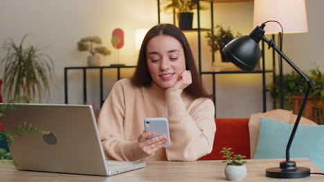 caucasian young woman sits at home table use smartphone share messages on social media application