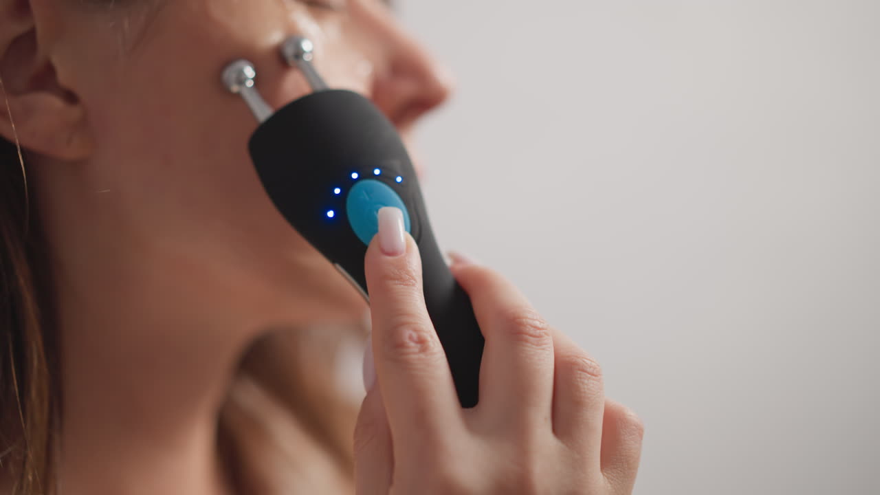 Woman uses microcurrent device with healing effect on skin. Female with manicure does microcurrent procedure for shining skin in shower slow motion